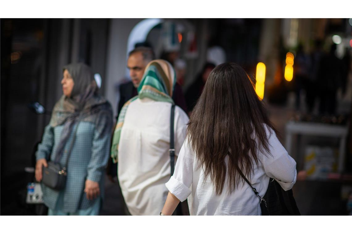 2023: Eine Frau läuft in Teheran mit offenen Abend am Abend eine Straße entlang.