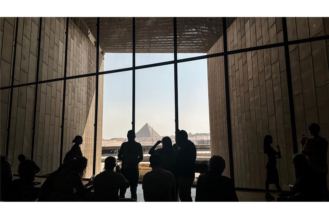 Besucher stehen vor einem Fenster mit Blick auf die Pyramiden von Gizeh im Großen Ägyptischen Museum (GEM).