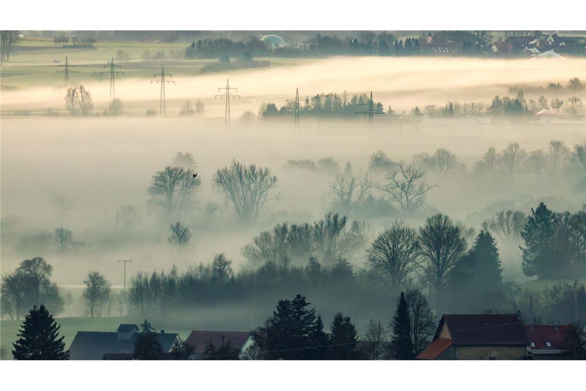 Bodennebel an der Donau hängt am Morgen bei Minusgraden im Gegenlicht der aufgehenden Sonne  in Riedlingen in Baden-Württemberg über der Landschaft.