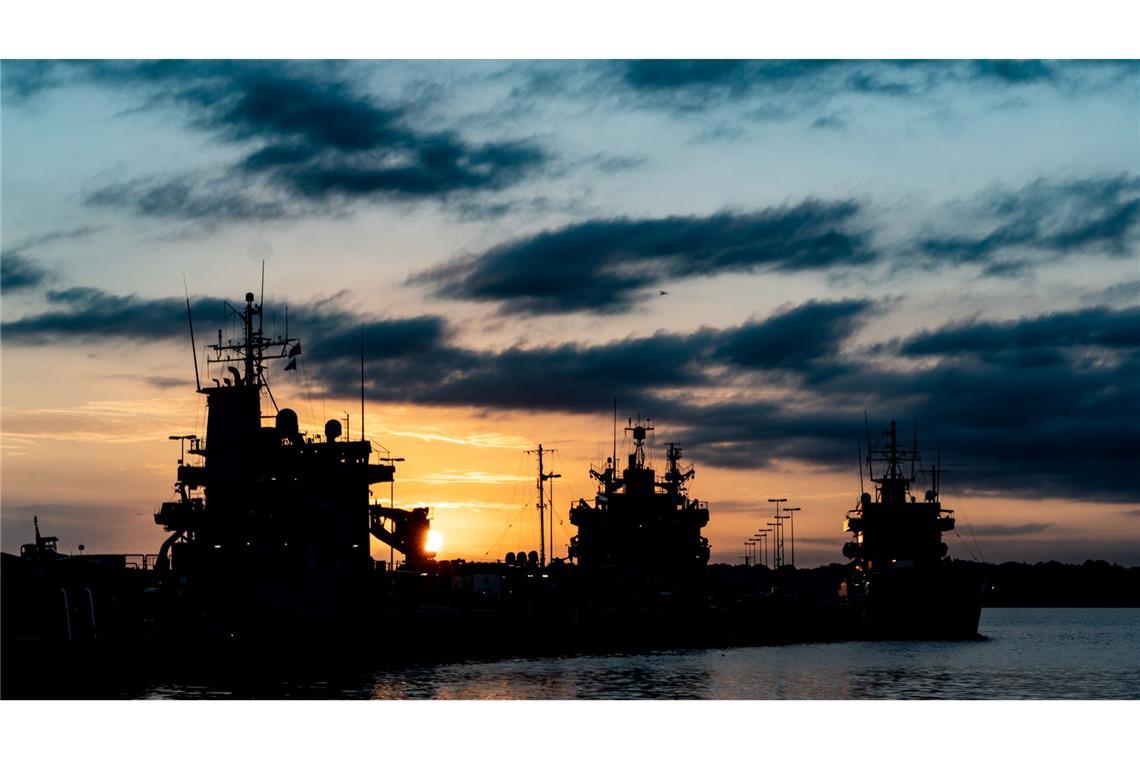 Die Sonne geht hinter dem Marinehafen in Kiel auf. Die Schiffe im Hafen sind im Gegenlicht nur als dunkle Silhouetten sichtbar.