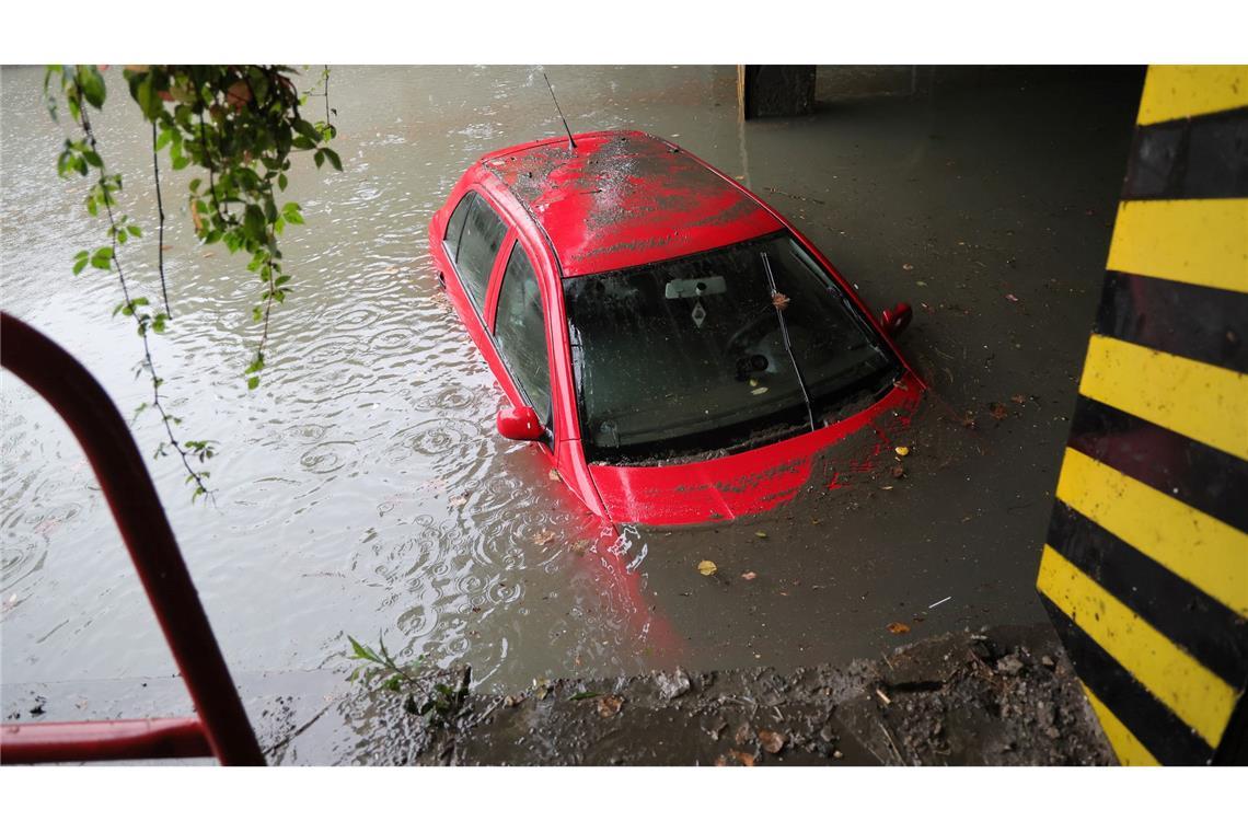 Ein Auto steht unter einer Bahnlinie in einer überfluteten Unterführung im Wasser.