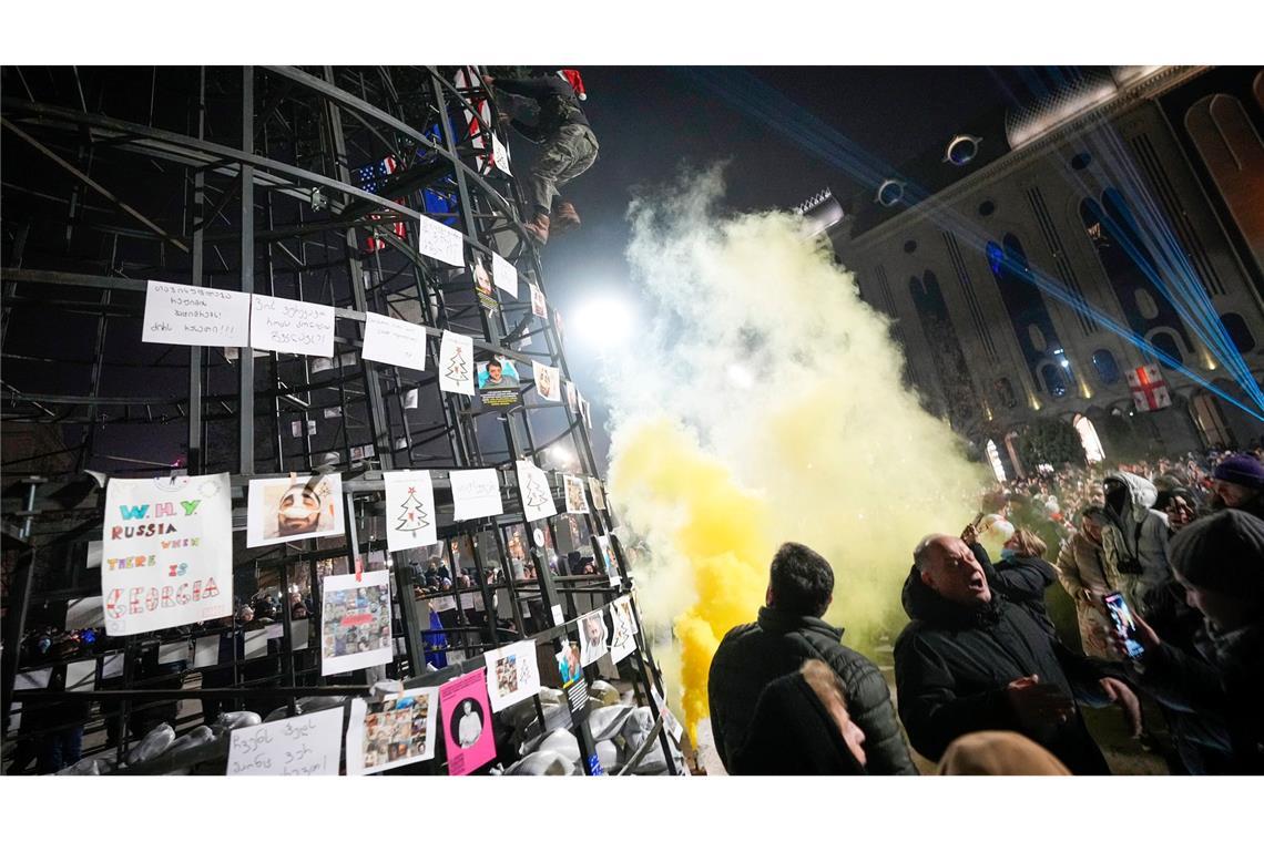 Ein Demonstrant befestigt eine georgische Flagge an einem vor dem Parlamentsgebäude aufgestellten künstlichen Weihnachtsbaum.