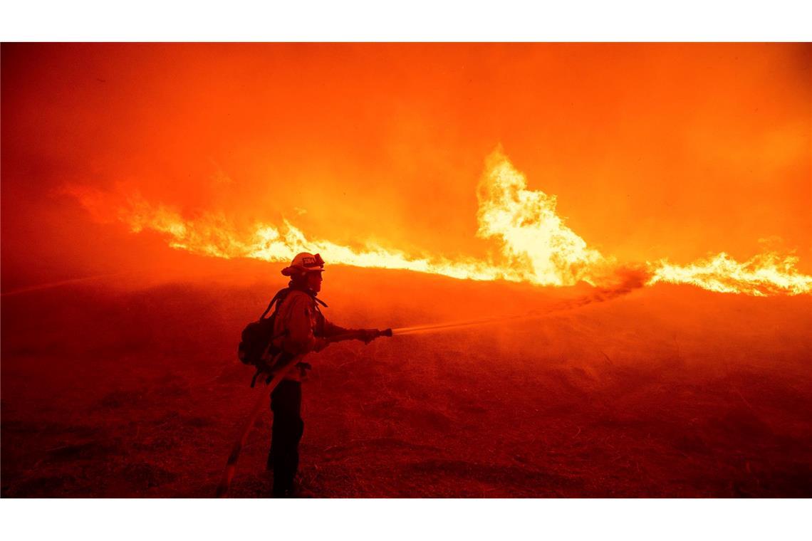 Ein Feuerwehrmann versprüht Wasser, während er die vom Hughes-Feuer in Kalifornien verursachten Flammen an einem Straßenrand überwacht.