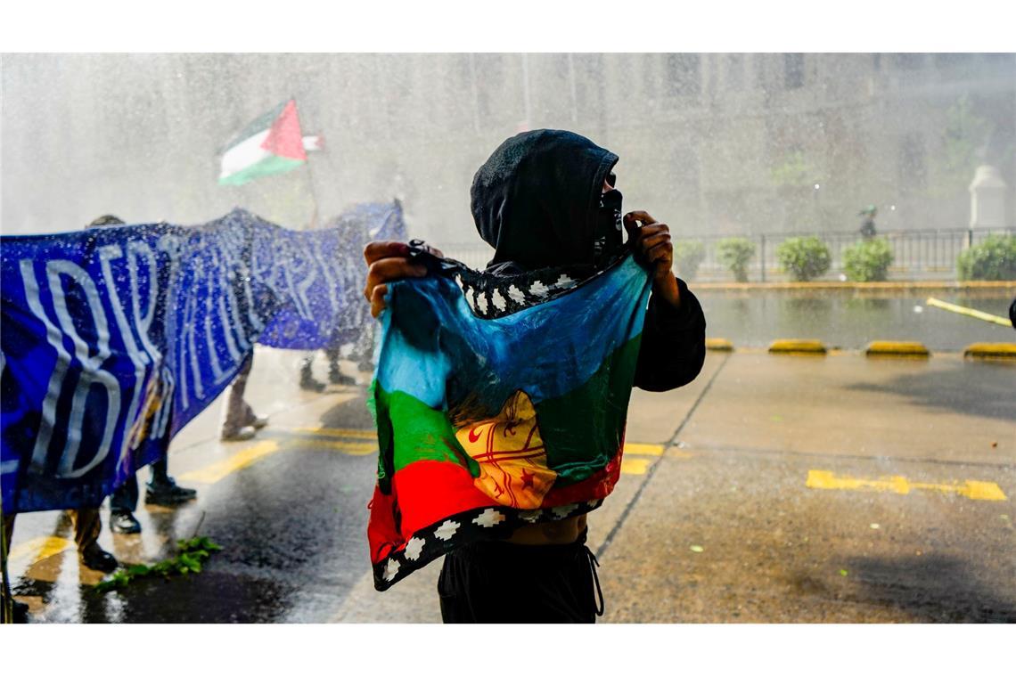 Ein Indigener hält eine Mapuche-Flagge, während die Polizei bei einem Marsch zur Forderung nach einem autonomen Territorium für Chiles Indigene und die Freilassung von Pro-Mapuche-Häftlingen Wasser und Tränengas auf Demonstranten schießt.