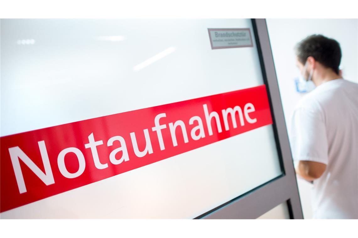 Ein Krankenpfleger steht in einem Krankenhaus neben einer Glastür mit der Aufschrift „Notaufnahme“.