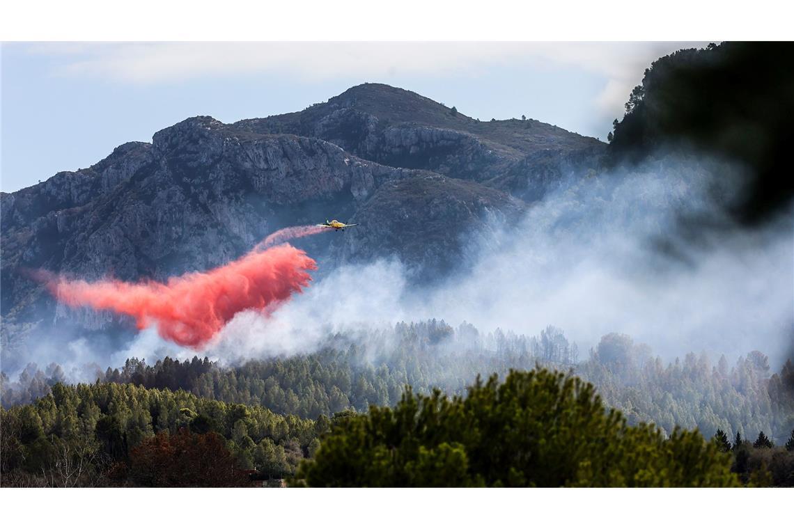 Ein Löschflugzeug wirft rotes Löschmittel über einem Waldbrand in Spanien ab.