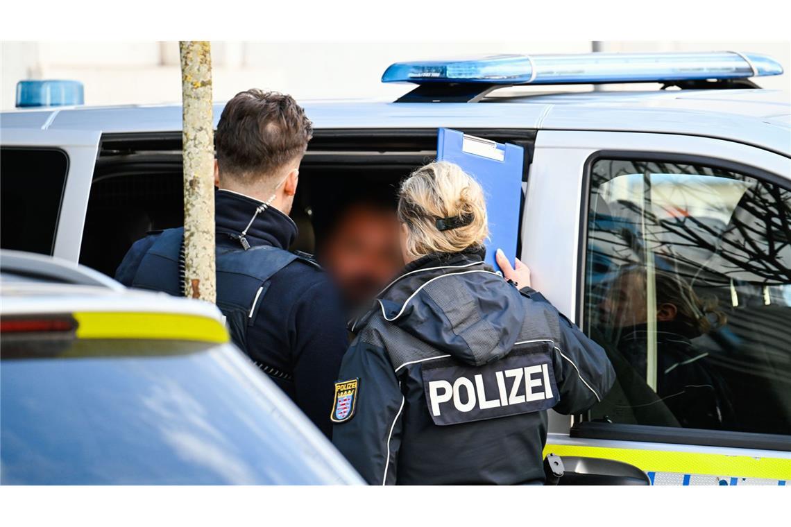 Ein Mann wird von Polizisten in einen Polizeiwagen gebracht.