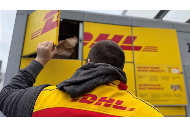 Ein Paketbote von DHL steht an einer Packstation, um diese mit Paketen zu befüllen (Symbolbild).