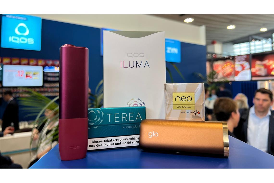 Ein Tabakerhitzer der Marke Iqos vom Hersteller Philip Morris und ein dazugehöriges Päckchen Tabaksticks der Marke Terea sowie das Konkurrenzprodukt Glo (mit Neo-Tabaksticks) des Herstellers BAT liegen bei der Fachmesse Intertabac in einer Messehalle.