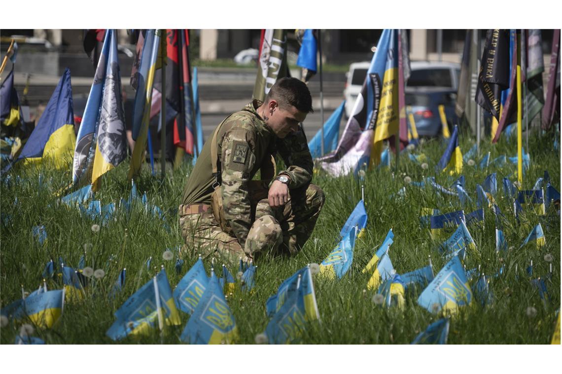 Ein ukrainischer Soldat legt auf dem Unabhängigkeitsplatz in Kiew eine kleine Nationalfahne auf den Rasen, um an einen Kameraden zu erinnern, der bei einem Gefecht mit russischen Truppen gefallen ist.