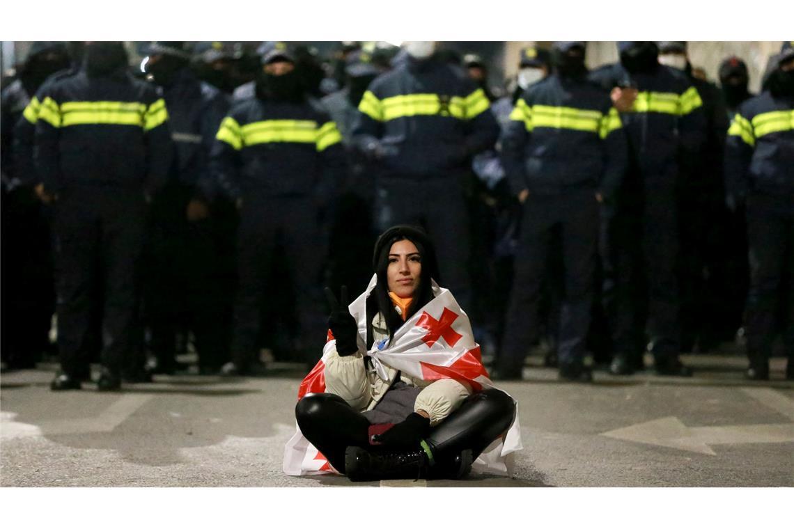 Eine Demonstrantin sitzt während der Proteste in Georgien vor Polizisten.