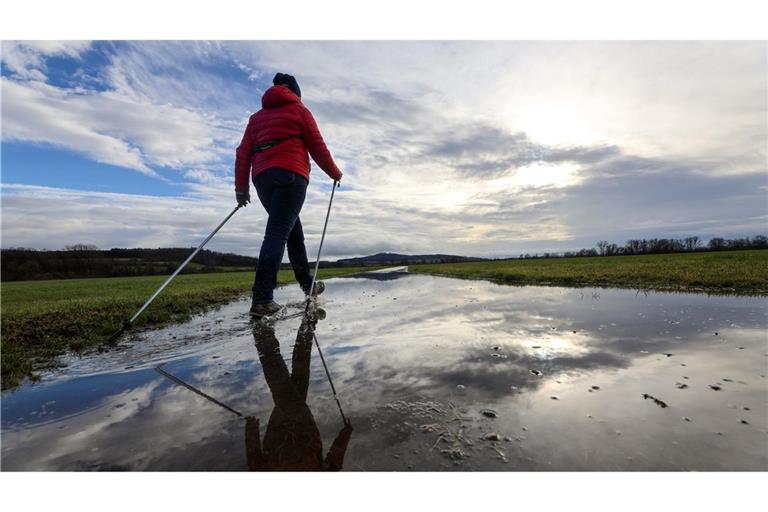 Eine Frau geht am vierten Advent mit Nordic Walking Stöcken durch eine Regenpfütze, in der sich der Himmel widerspiegelt.