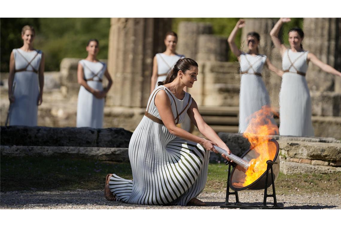 Eine Schauspielerin in einem Priesterinnen-Gewand entzündet die olympische Flamme mithilfe eines Spiegels.