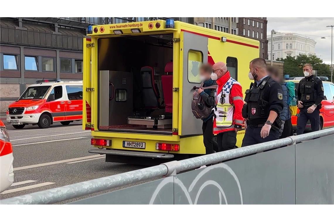 Einsatzkräfte mit Mundschutz begleiten zwei Menschen zum Rettungswagen der Feuerwehr vor dem Hauptbahnhof.