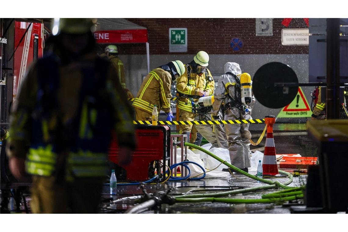 Feuerwehrleute in Schutzkleidung stehen auf dem Gelände eines Chemiebetriebs bei einem Brand in Duisburg.