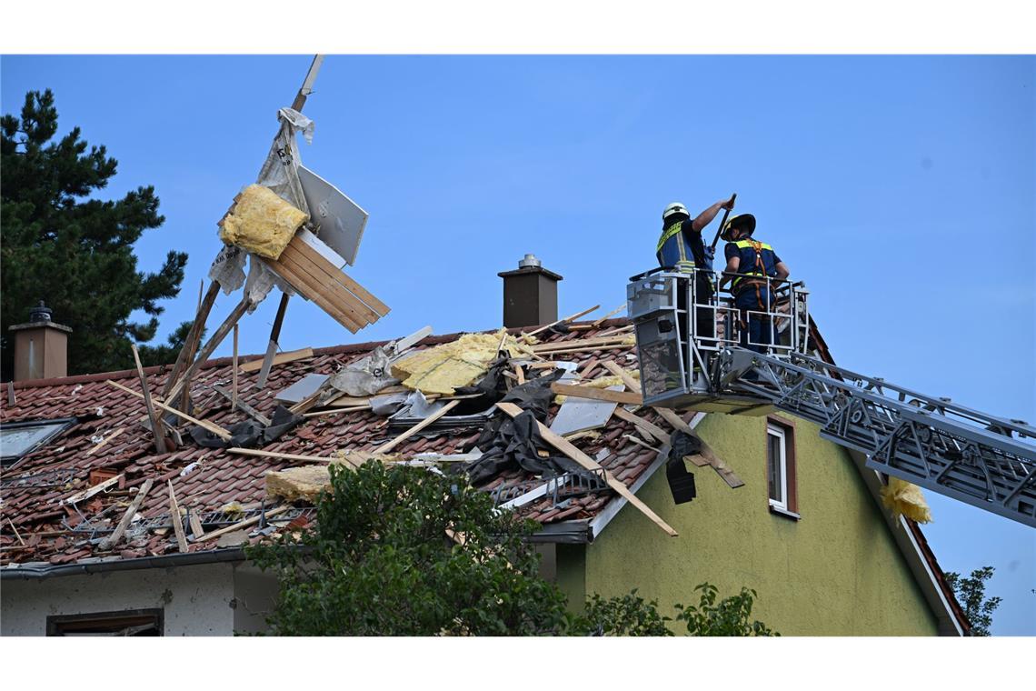 Feuerwehrleute räumen Trümmer vom Dach eines Hauses.