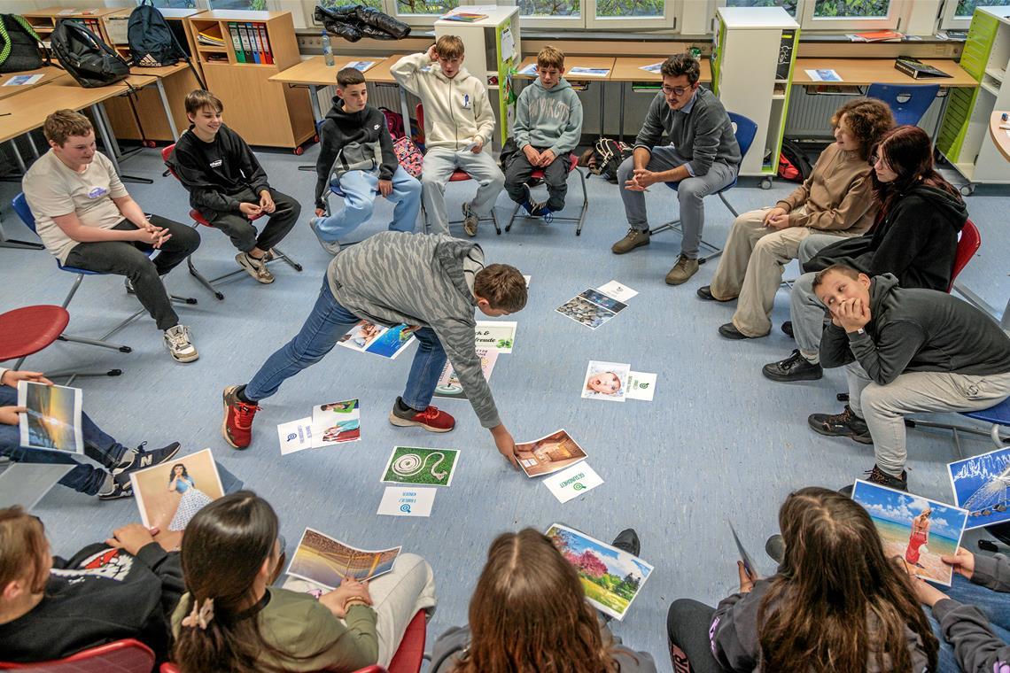 Im Kurs „Glück und Lebenszufriedenheit“ mit Konrektor Kai Kasper (hinten rechts) schauen sich die Schülerinnen und Schüler ihre Lebensziele an. Sie haben sich aus einem größeren Fundus für sie passende Bilder ausgesucht und sprechen darüber, was sie erreichen möchten. 