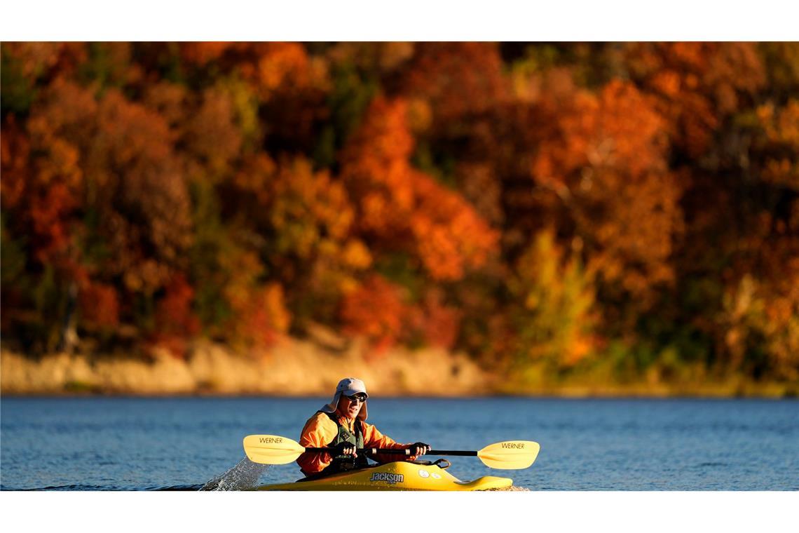 Indian Summer in den USA: Ein Mann fährt in Kansas mit dem Kajak an Bäumen vorbei, die in bunten Herbstfarben leuchten.