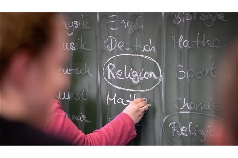 ine Lehrerin schreibt mit Kreide einen Stundenplan mit Religionsunterricht an eine Tafel.