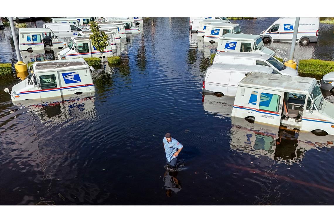 Knietief im Wasser: Ein USPS-Mitarbeiter inspiziert Fahrzeuge, nachdem heftige Regenfälle des Hurrikans "Milton" den Anclote River überflutet haben.