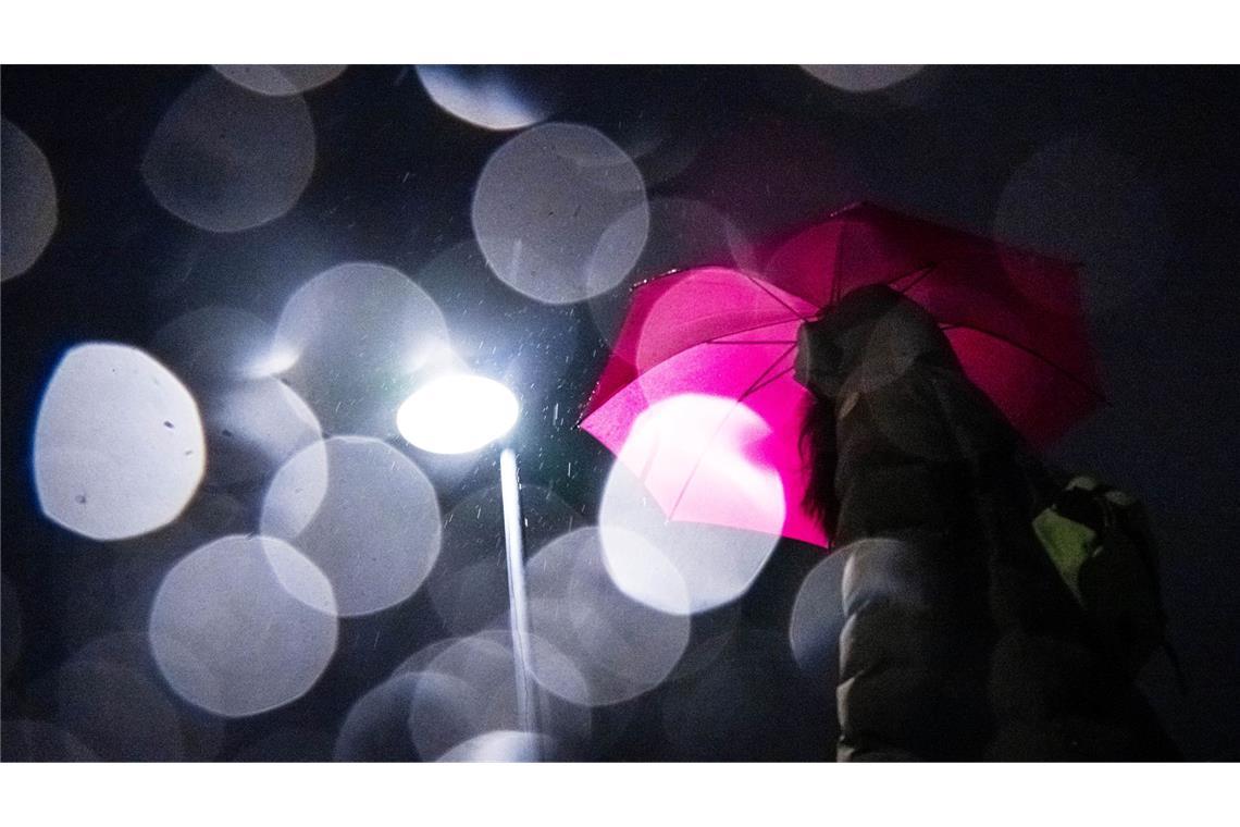 Lichtspiel in der Dunkelheit: Eine Frau mit Regenschirm geht am frühen Morgen in Bremen über eine Brücke über die Weser.