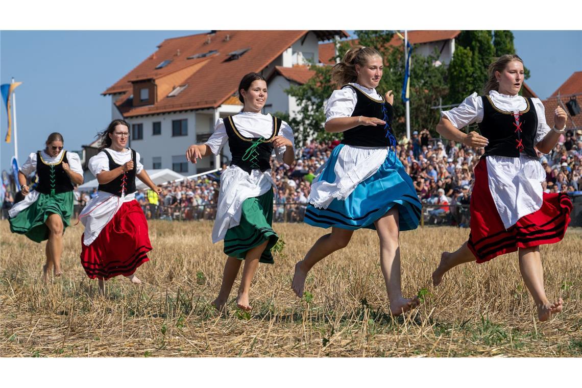 Mit wehenden Dirndln laufen junge Frauen in Markgröningen (Baden-Württemberg) beim historischen Schäferlauf barfuß auf dem Stoppelfeld.