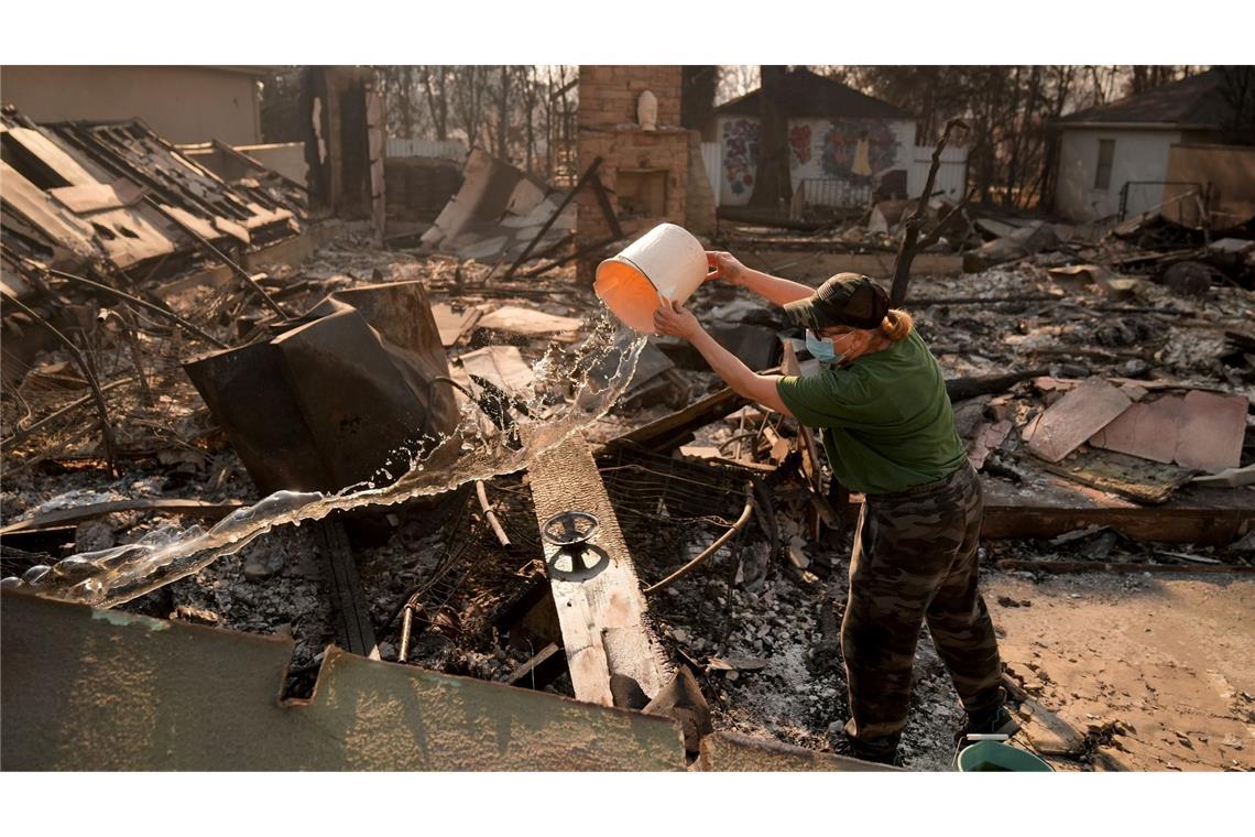 Nancy Belanger gießt Wasser auf das vom Feuer verwüstete Grundstück eines Nachbarn im Stadtteil Pacific Palisades von Los Angeles.