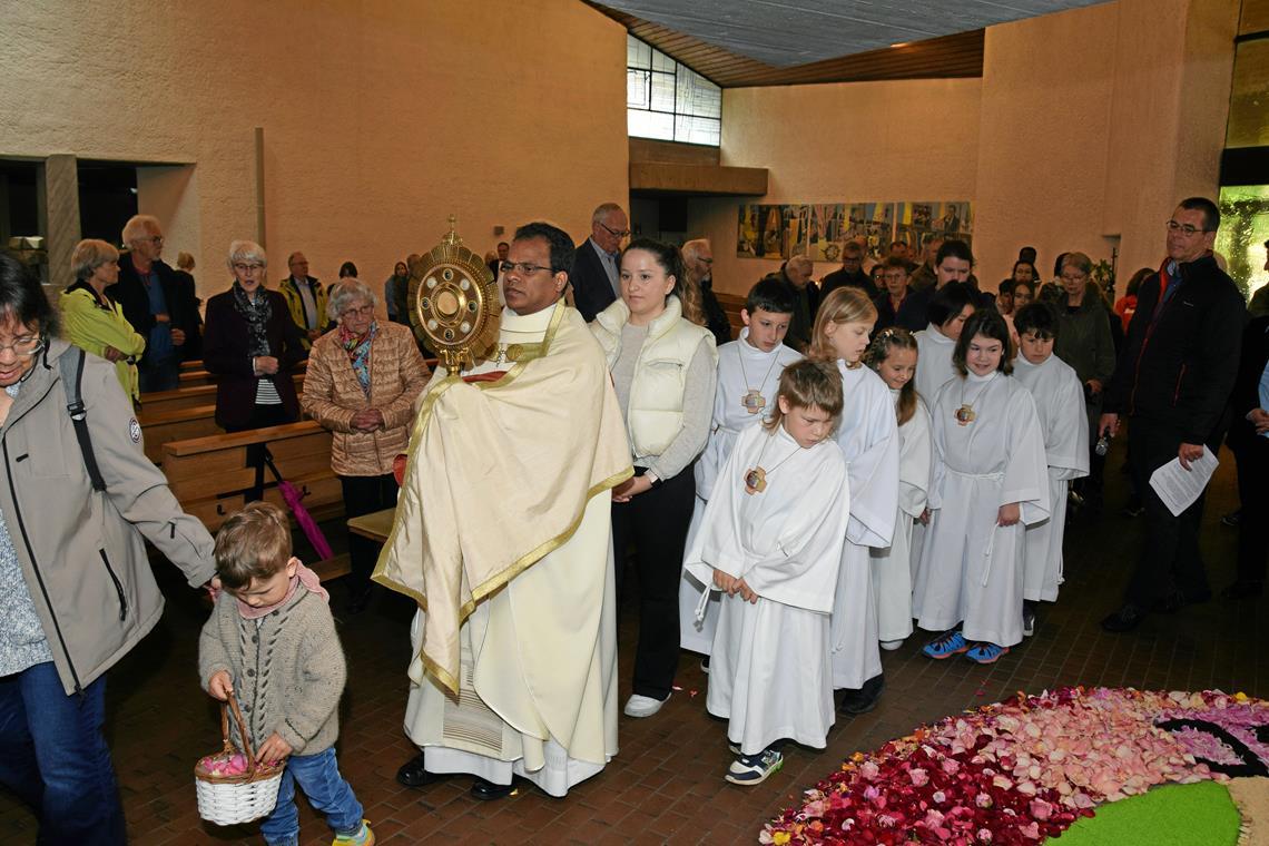 Pfarrer Jose Antony O.Praem (Mitte) schreitet mit der Monstranz voran, es folgen – vorbei am und beeindruckt vom Blumenteppich – Ministrantinnen, Ministranten und Lektoren sowie Mädchen und Jungen, die dieses Jahr Erstkommunion gefeiert haben. Fotos: Elisabeth Klaper