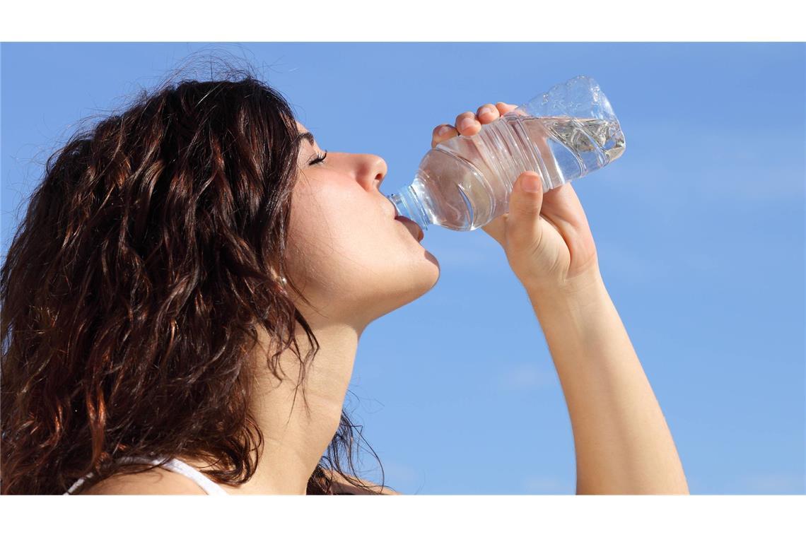 Profil einer Frau, die Wasser aus einer Plastikflasche trinkt. Im Hintergrund ist ein blauer Himmel zu sehen (Symbolfoto).