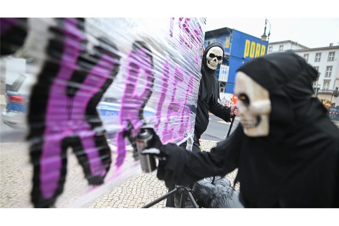 Protestaktion gegen Krieg: Eine Frau mit einer Totenkopfmaske sprüht während einer Aktion vor der russischen Botschaft gegen den russischen Angriffskrieg in der Ukraine eine Parole auf ein Transparent.