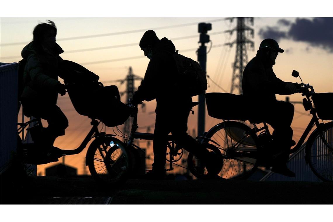 Schattenrisse: Menschen fahren in der Abenddämmerung in Yokohama in der Nähe von Tokio mit Fahrrädern im Gegenlicht der Abendsonne.