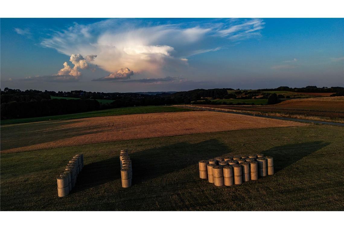 Strohballen liegen in der Abendsonne auf einem Feld, während sich Wolken am Himmel bilden.