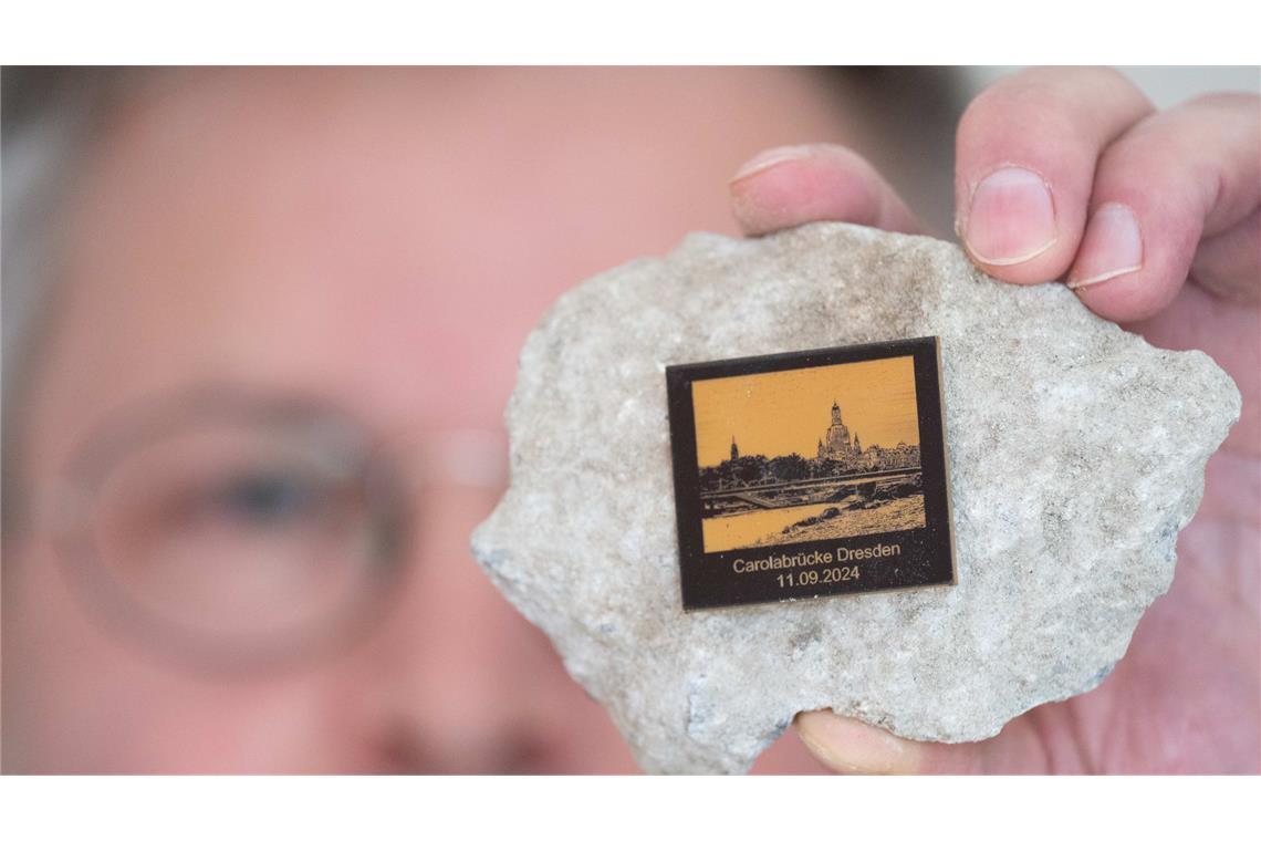 Torsten Daae, Geschäftsführer im Dresdner Laden "Catapult", hält einen Stein des abgerissenen Brückenteils der eingestürzten Carolabrücke mit einer Plakette in der Hand.