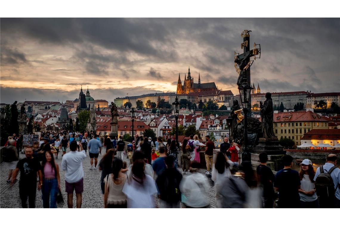 Touristen gehen im Abendlicht über die Karlsbrücke in Prag.