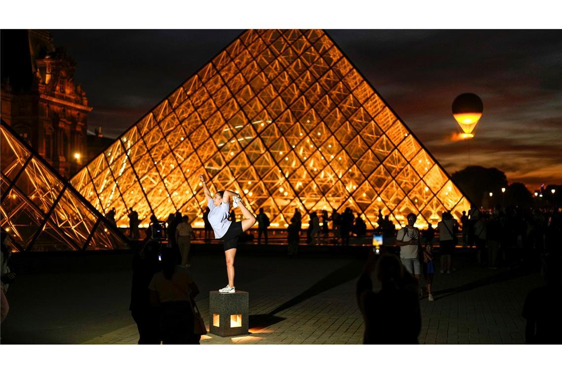 Turnübungen und Fotos in der Nähe an den Pyramiden am Louvre, während das olympische Feuer in Hintergrund aufsteigt.