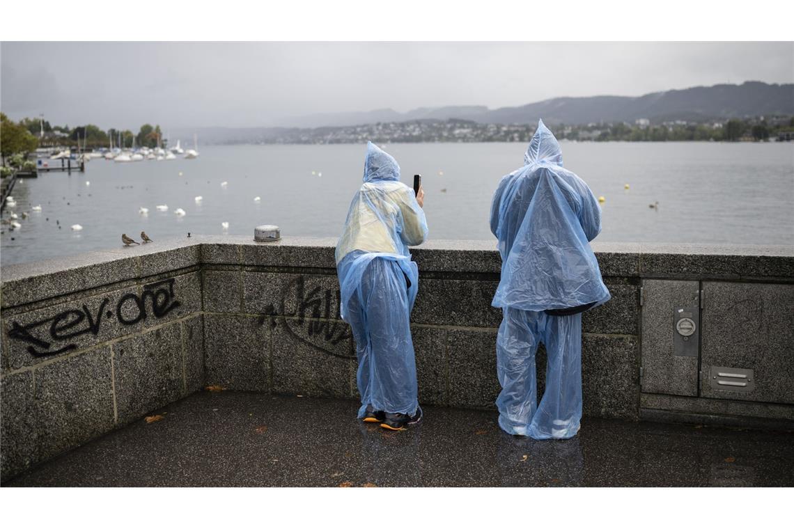 Verregneter Urlaub: Ganzkörperregenmontur tragen zwei Touristen am Zürichsee in der Schweiz.