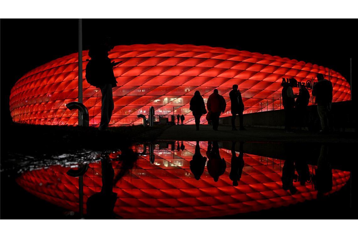 Vor dem Spiel von Bayern München gegen Paris Saint-Germain kommen Zuschauer an der Arena an, die im Dunkeln rot beleuchtet wird.