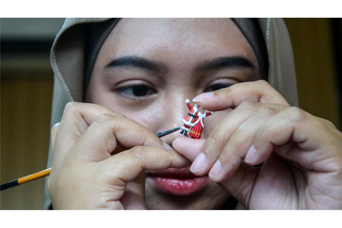 Weihnachtsfiguren in Indonesien: eine Frau bemalt eine weihnachtliche Miniaturfigur in einer Werkstatt.