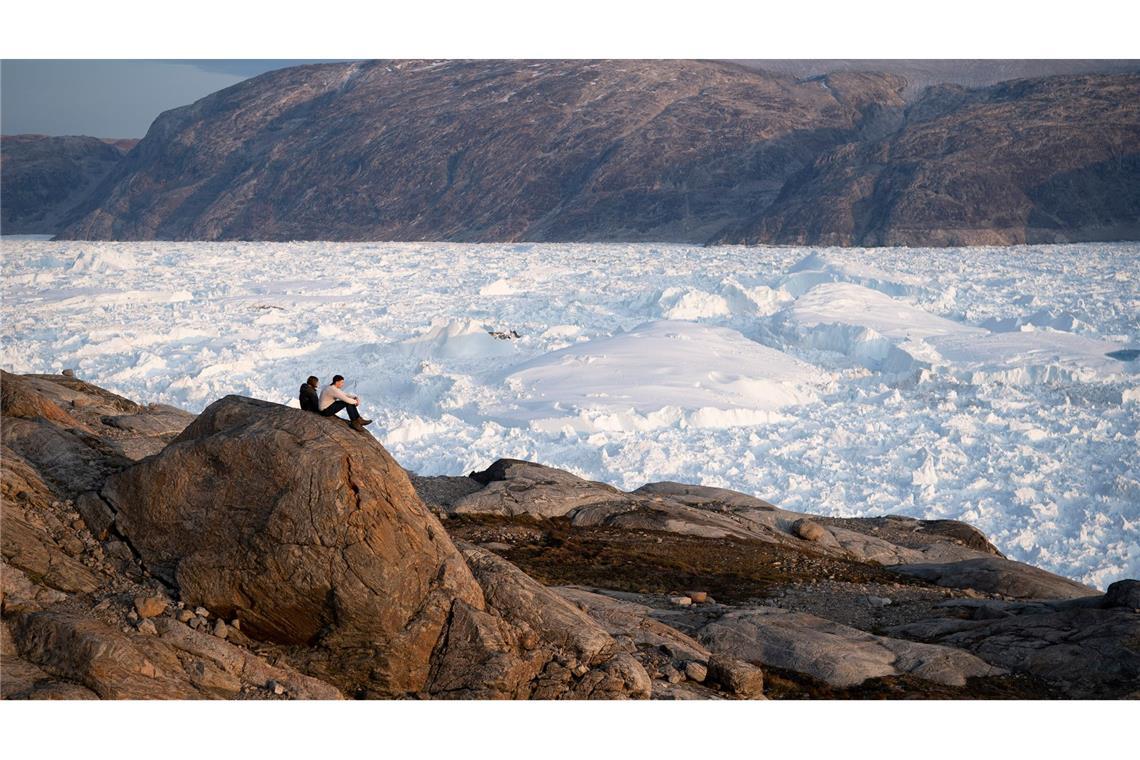 Zwei Studenten der New York University sitzen auf einem Felsen mit Blick auf den grönländischen Helheim-Gletscher.